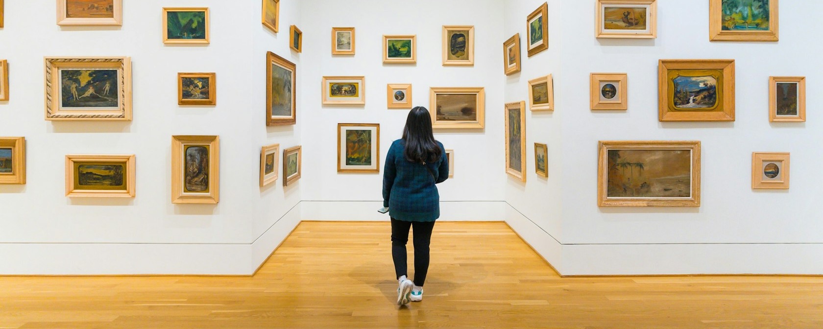 Un visiteur explore une galerie de la collection Phillips, où de petites peintures encadrées de styles variés sont disposées sur des murs blancs, créant une expérience artistique immersive.